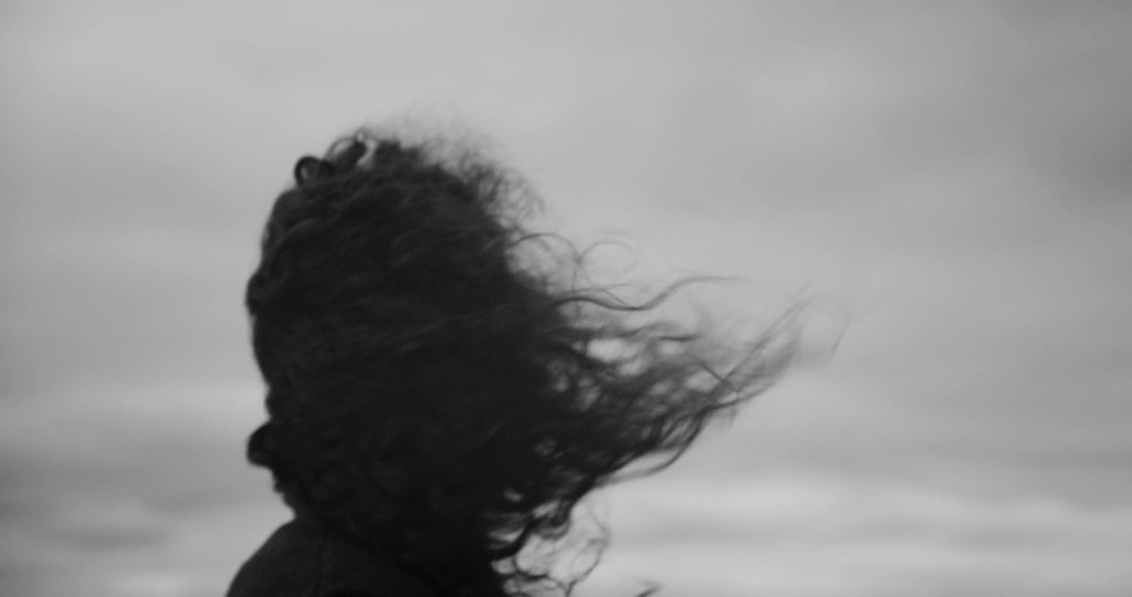 The woman seen from behind, her dark curly hair blown by the wind. From A Drop at a Time (2025), directed by Mazyar Mahan.