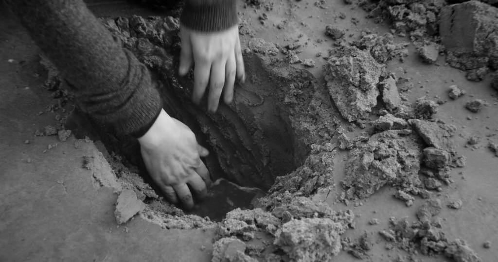 Close-up of hands digging a hole in hard, cracked earth. From A Drop at a Time (2025), directed by Mazyar Mahan.