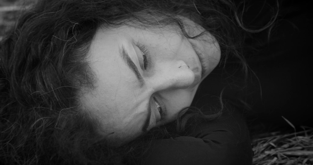 Close-up of the exhausted woman lying on the ground, her face pressed to the dry grass. From A Drop at a Time (2025), directed by Mazyar Mahan.