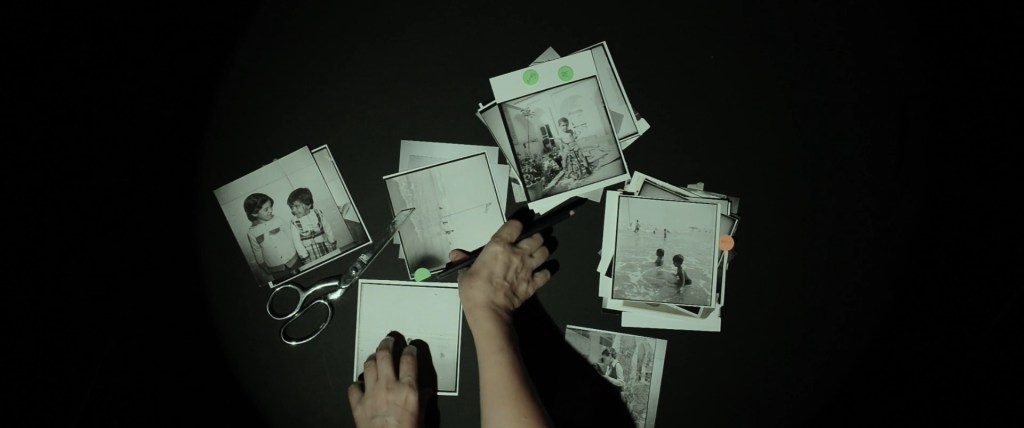 Still from Exile Echoes (2024) by Mazyar Mahan: seen from above, hands sort old black-and-white photographs on a dark table.