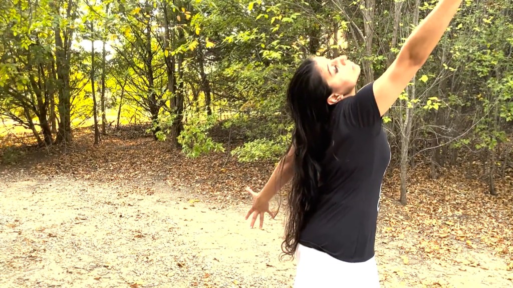 Still from For Freedom (2022) by Mazyar Mahan: the dancer reaches up toward the sunlit trees.
