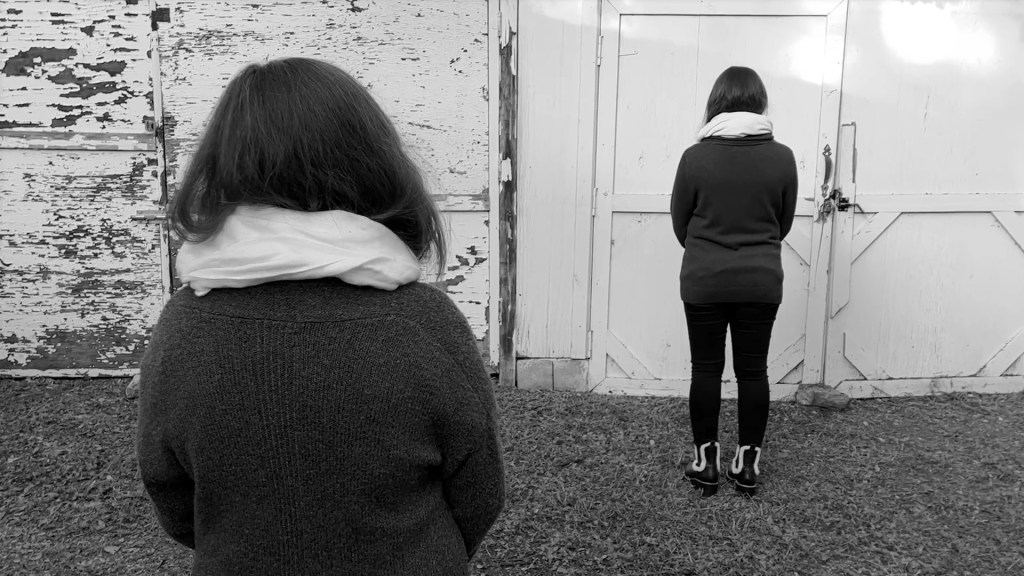 Still from Return of the Repressed (2023) by Mazyar Mahan: two women stand facing a weathered white door