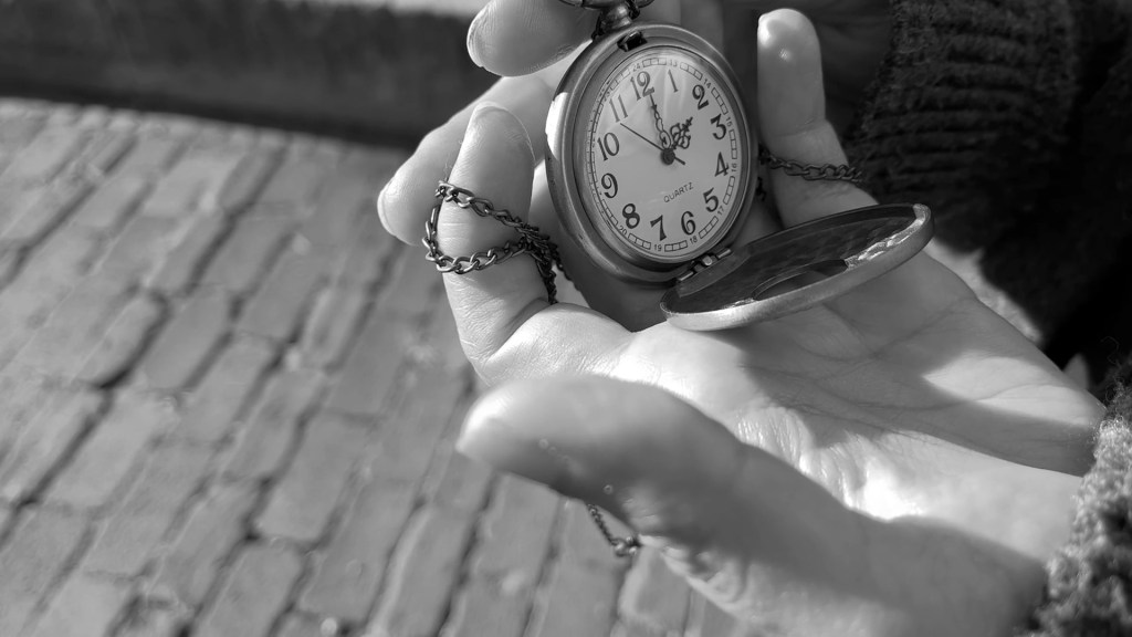 Still from Return of the Repressed (2023) by Mazyar Mahan: an open pocket watch in an outstretched hand above the brick pavement.