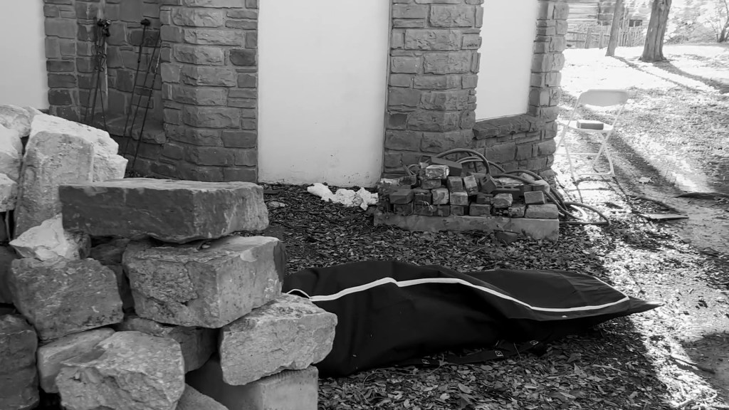 Still from Return of the Repressed (2023) by Mazyar Mahan: a black bag lies beside a pile of stones in the afternoon light.